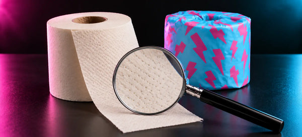 Magnifying glass over a cream toilet paper sheet beside an unwrapped roll and a cyan wrapper with pink lightning bolts.