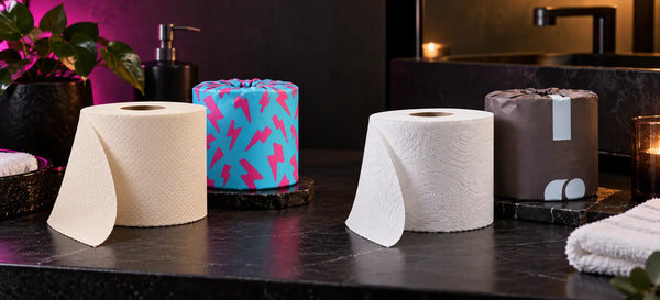 Cream Skid Slayer toilet paper with a cyan-pink lightning wrapper beside a white toilet paper roll and brown wrapper on a bathroom counter.