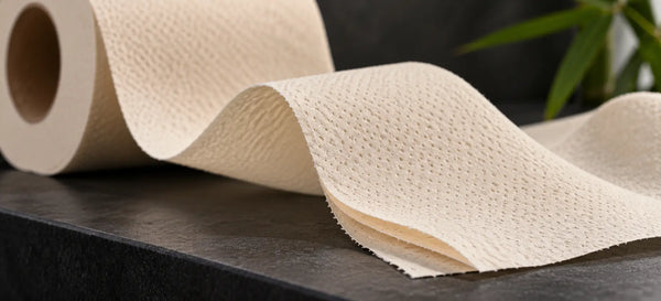 Close-up of cream bamboo toilet tissue with soft folds, fine embossed texture and separated layers on a dark counter.